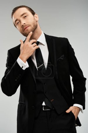 Ein gutaussehender, bärtiger Geschäftsmann im Anzug posiert selbstbewusst vor grauer Studiokulisse.