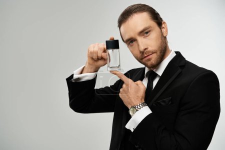A handsome, bearded businessman in a suit elegantly holds a glass bottle with perfume