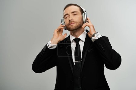 A bearded businessman in a suit is attentively listening to headphones against a grey studio backdrop.