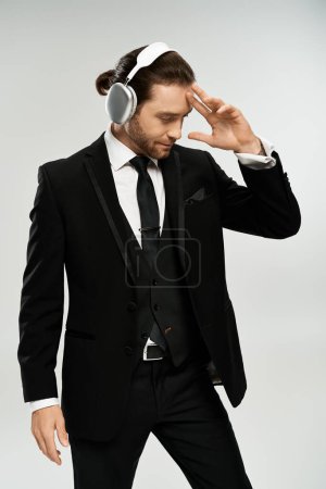 Foto de Un hombre de negocios barbudo y guapo con un traje escuchando música con auriculares en un estudio sobre un fondo gris. - Imagen libre de derechos