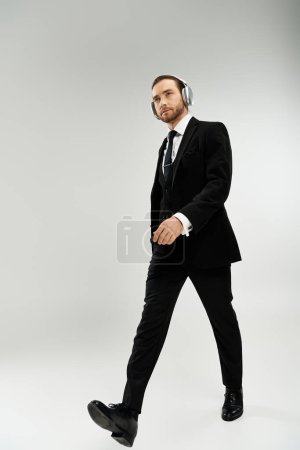 Téléchargez les photos : A bearded businessman in a suit walks confidently wearing headphones. - en image libre de droit