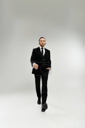 Foto de Un hombre de negocios guapo y barbudo con traje y corbata camina con confianza en un estudio sobre un fondo gris. - Imagen libre de derechos