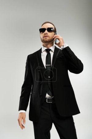 Bearded businessman in a sleek suit and sunglasses conversing on a cellphone, exuding confidence and professionalism.