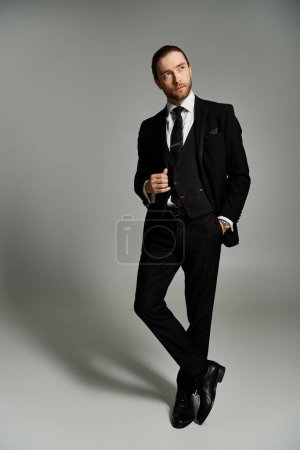 A handsome, bearded businessman confidently poses in a stylish tuxedo against a grey studio background.