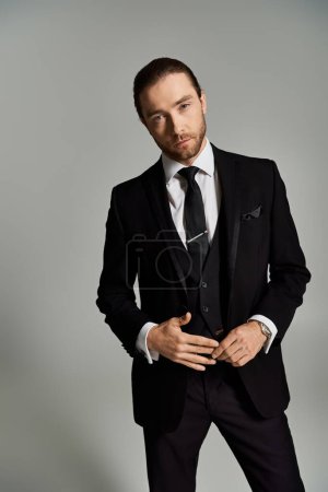 A stylish gentleman in a suit and tie confidently poses for a portrait in a studio setting against a grey background.
