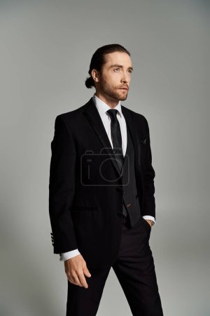 Téléchargez les photos : Un bel homme d'affaires barbu en costume et cravate frappant une pose confiante dans un décor de studio sur un fond gris. - en image libre de droit