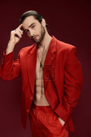Ein gutaussehender Mann posiert selbstbewusst in einem auffallend roten Anzug ohne Hemd in einem professionellen Studio-Setting.
