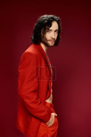 Handsome man in a red suit without a shirt striking a confident pose in a studio setting.
