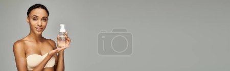 Photo for Young African American woman with facial cleanser on a grey background. - Royalty Free Image
