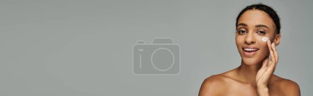 Eine schöne junge Afroamerikanerin in einem schulterfreien Oberteil, verziert mit lebendigem Make-up, auf grauem Hintergrund.
