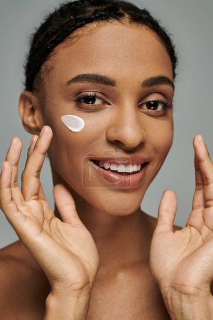 Photo for Young African American woman applying cream to her face, focused on skincare routine, exuding confidence and beauty. - Royalty Free Image