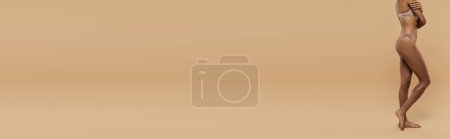 Photo for A stunning African American woman in a bikini gracefully holds an umbrella against a beige backdrop. - Royalty Free Image