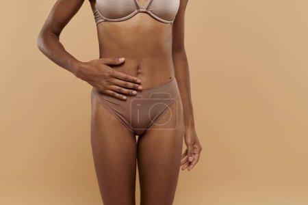 Eine hübsche, schlanke Afroamerikanerin im Bikini posiert anmutig vor beigem Hintergrund.