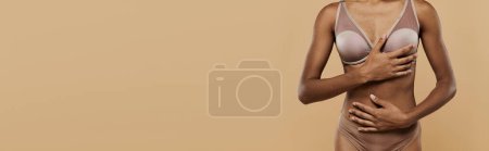 A stunning African American woman exuding confidence poses in a bikini on a beige background.
