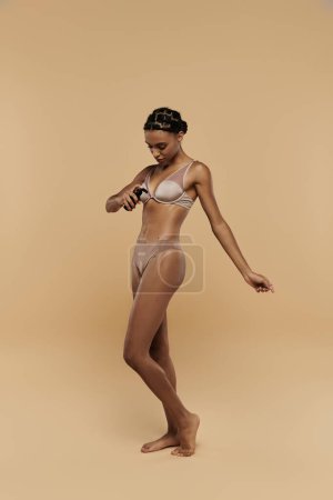Beautiful, slim African American woman standing confidently in a bikini against a beige backdrop.