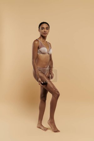 Foto de Una esbelta mujer afroamericana se para con confianza en un bikini sobre un fondo beige neutro. - Imagen libre de derechos