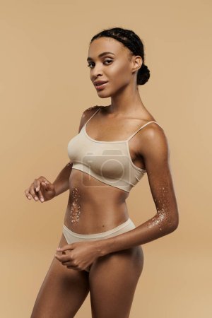 Afroamerikanerin trägt ein Bikini-Oberteil und Höschen mit Anmut und Selbstbewusstsein auf neutralem Hintergrund.