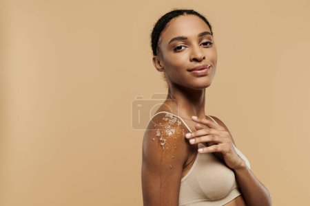 African American woman in underwear, gracefully adorned with scrub, on beige background.