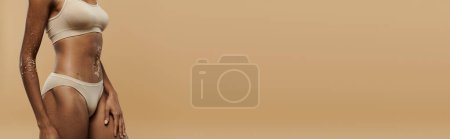 Photo for African American woman in a white bikini top strikes a confident pose against a beige backdrop. - Royalty Free Image