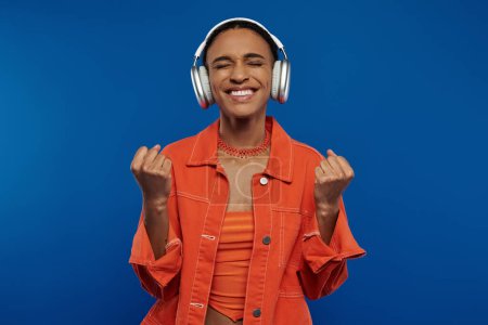 A young African American woman in a bright orange shirt listens to music on headphones.