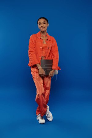 A woman in an orange jumpsuit holding a laptop.