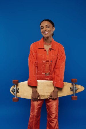 A woman in an orange shirt confidently holds a skateboard.