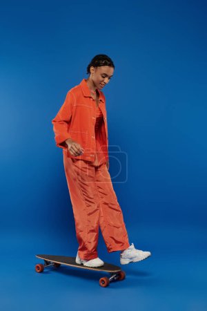 A woman in an orange jumpsuit effortlessly rides a skateboard, showcasing skills and freedom of movement.