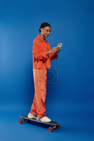 Eine lebhafte junge Afroamerikanerin in orangefarbenem Outfit steht auf einem Skateboard und blickt auf ihr Handy..
