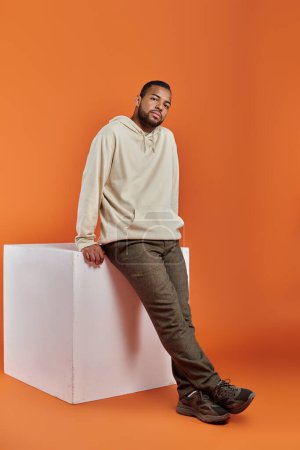 Stylish African American man posing on white box against vibrant background.