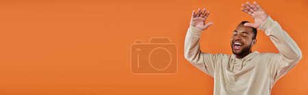Téléchargez les photos : Un homme afro-américain élégant lève joyeusement les mains sur un fond vibrant. - en image libre de droit