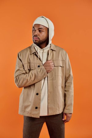 Photo for African American man posing in tan jacket and white hoodie against vibrant backdrop. - Royalty Free Image