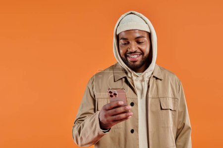 African American man in hoodie absorbed by smartphone, colorful background.
