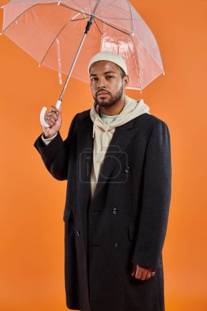 African American man in coat and hat holding umbrella.