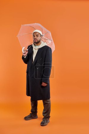 African American man stylishly holding umbrella against vibrant backdrop.