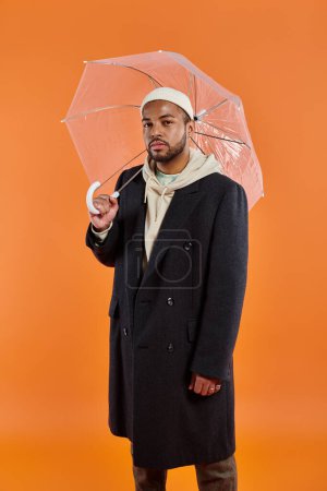 Stylish African American man in coat with umbrella.