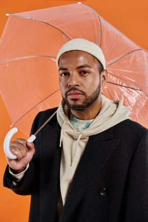 African American man stylishly poses under an umbrella.