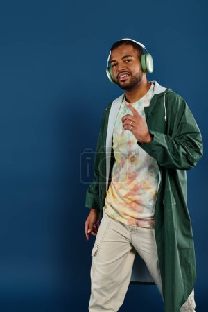 Photo for A stylish African American man wearing headphones poses against a vibrant blue backdrop. - Royalty Free Image