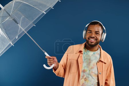 Foto de Elegante hombre afroamericano con auriculares sosteniendo un paraguas bajo un vibrante telón de fondo. - Imagen libre de derechos