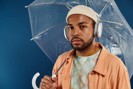 Hombre con estilo con auriculares que sostienen el paraguas contra el telón de fondo vibrante.