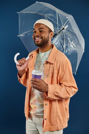 Afroamerikaner hält Regenschirm in der Hand und genießt Kaffee.