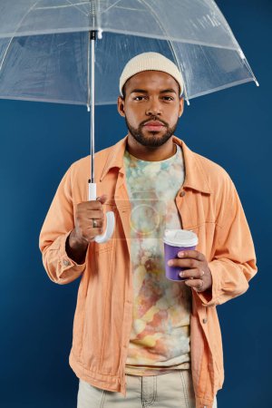 Fashionable African American man holding an umbrella and a cup of coffee.