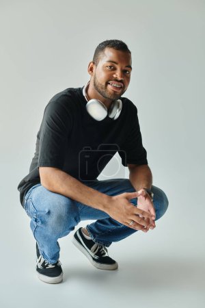 An African American man kneeling with headphones on a vibrant backdrop.