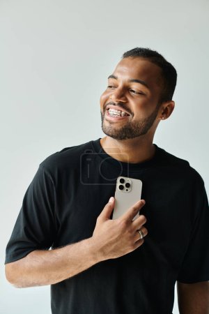 Elegante hombre afroamericano riendo mientras sostiene un teléfono celular.