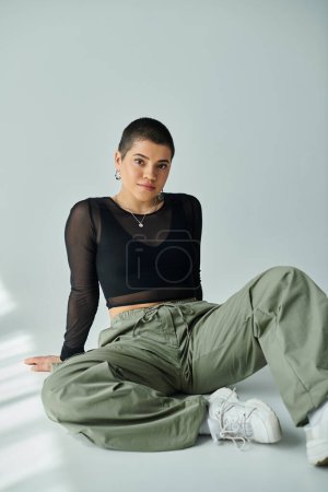 A young woman with short hair sits gracefully on the floor, exuding calmness and reflection.