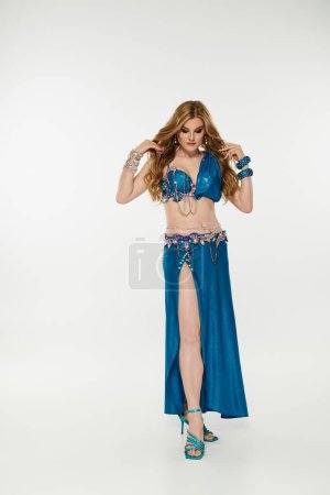 A graceful young woman in a vibrant blue belly dance costume sways elegantly.
