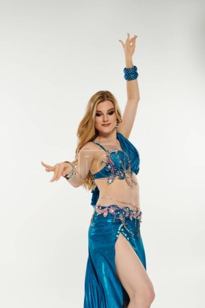 A captivating woman in a vibrant blue belly dance outfit showing fluid movements.