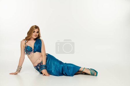 Elegant woman in blue dress gracefully lying on ground after belly dance.
