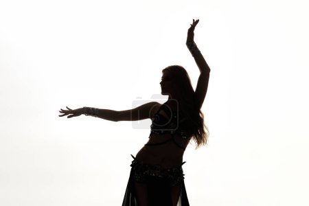 A woman in a belly dance pose with her arms raised gracefully.