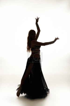 A captivating young woman in a black dress swirls gracefully while performing a belly dance.