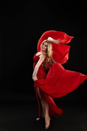 A captivating young woman in a red dress performs a mesmerizing dance.